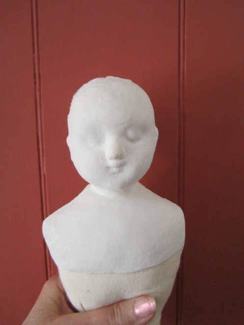 Photo of an uncleaned, unpainted  composition head mounted on a stuffed body with custom fitted shoulders.